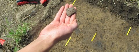 student holds artifact at archaeological dig site