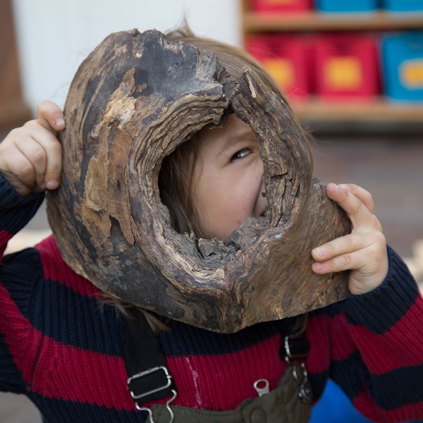 child looks through knot in piece of wood