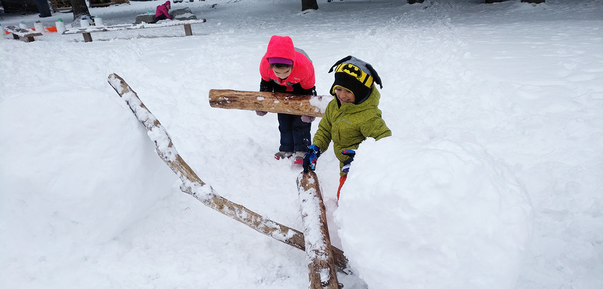Nature School students grab logs and branches to lift large ball of snow