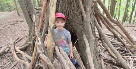 young boy builds a shelter of sticks and logs