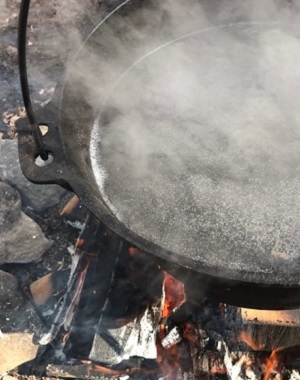 kettle filled with sap boils over a fire