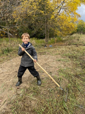 Nature School student using a rake to clear the overgrown sandbox at Kortright Centre